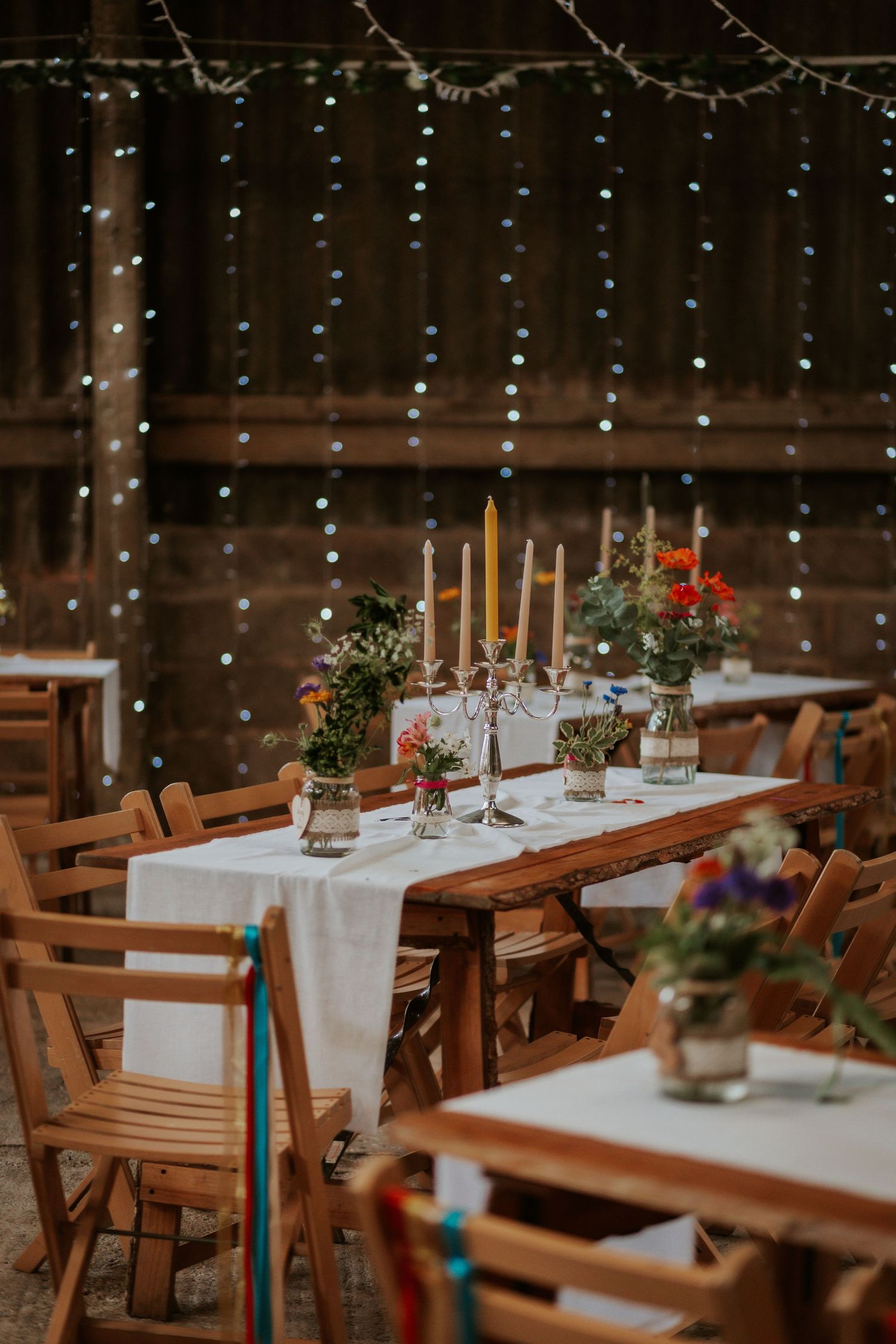 Rustic wedding table setting with candles and string lights in a barn venue.