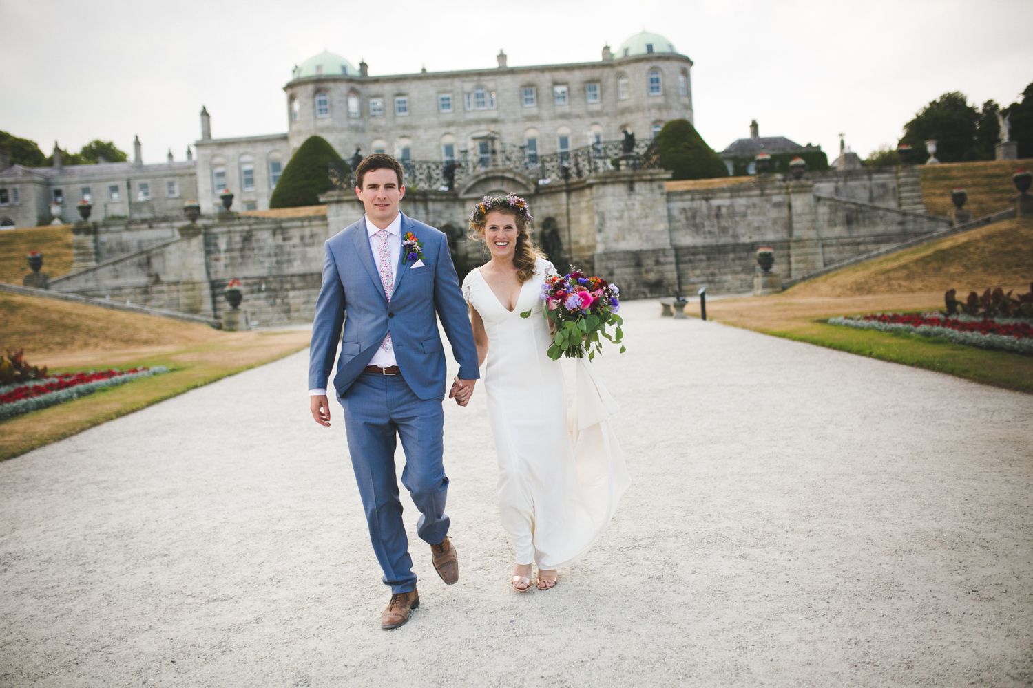 A newly married couple walking along a path at a grand manor estate.
