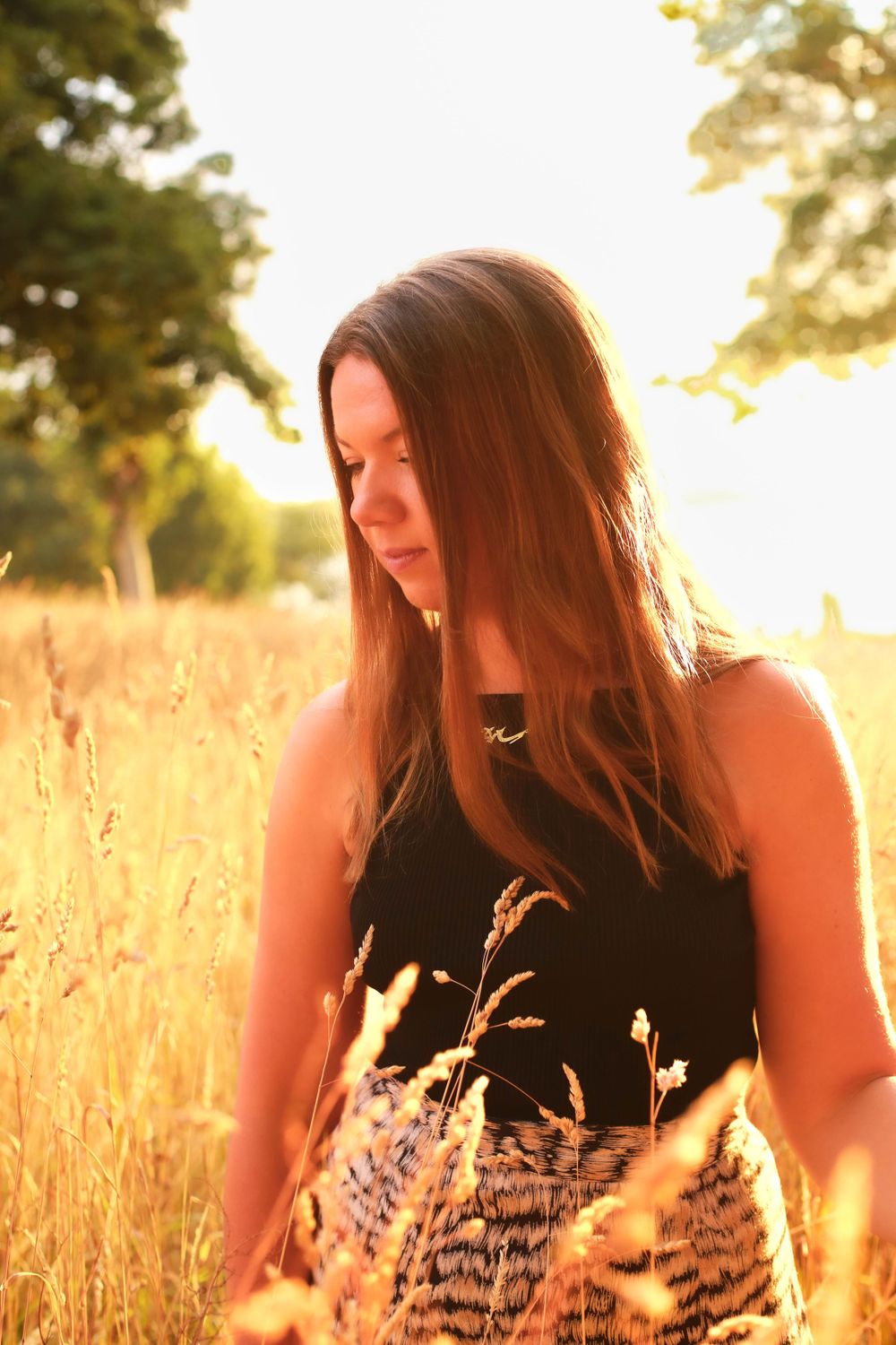 Person in black top standing in golden wheat field at sunrise with backlighting.