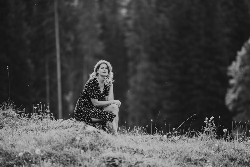 A silhouette sits on a grassy hillside against a backdrop of dark forest.
