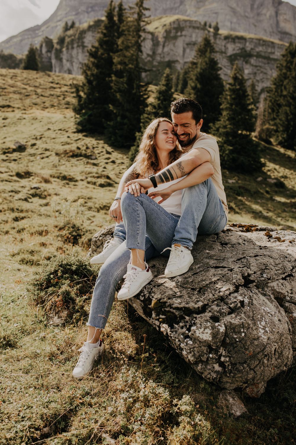 A couple sharing an intimate moment while sitting on a rock in a scenic mountain landscape.
