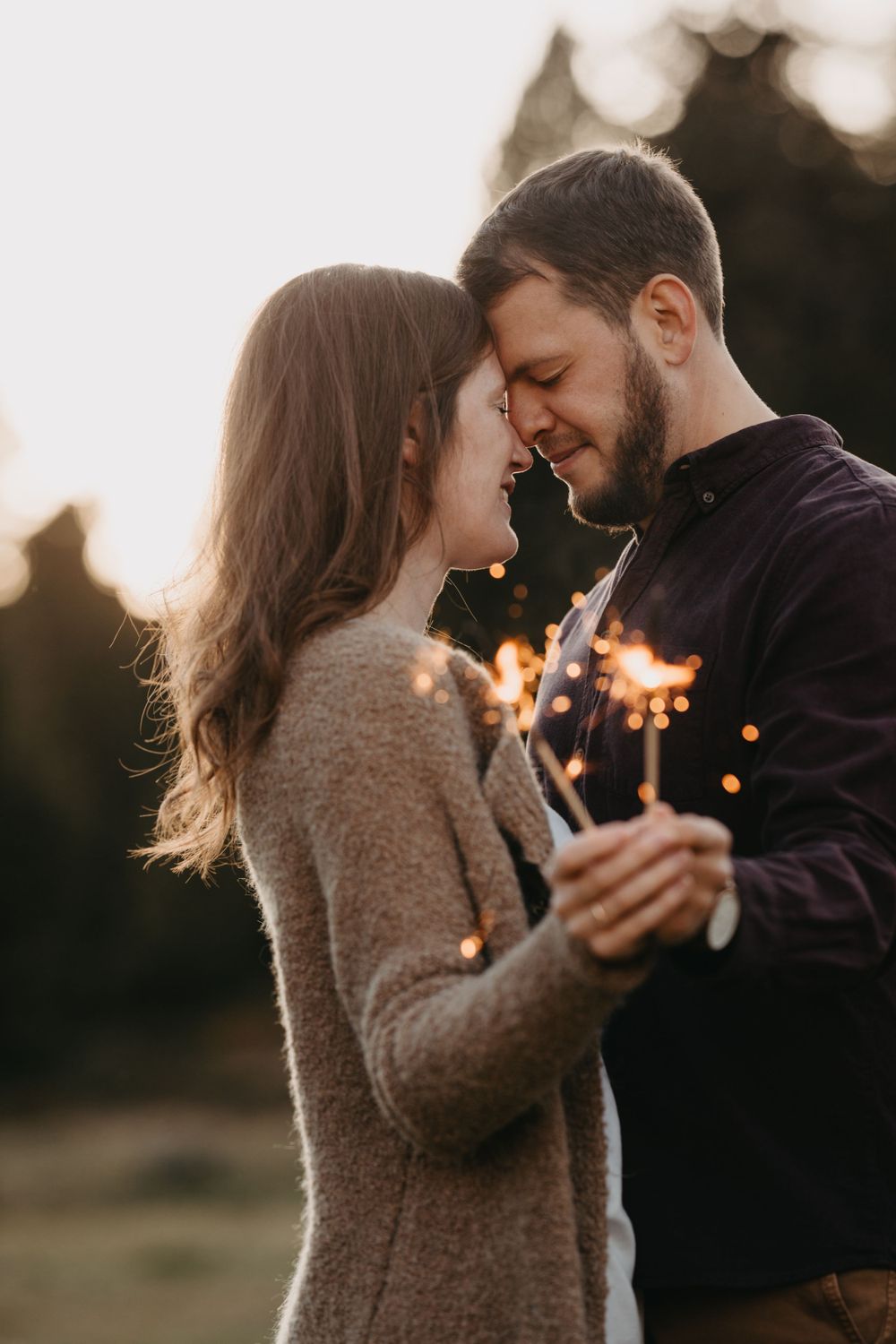 Romantic couple holding sparklers at sunset in warm winter clothing.