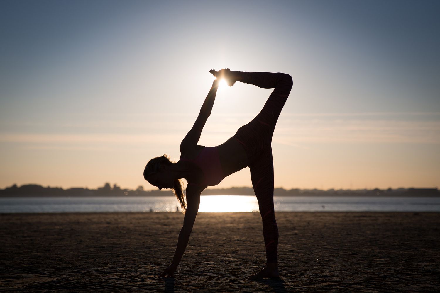 Silhouette of person performing half moon yoga pose at sunset by the water during business branding photoshoot.