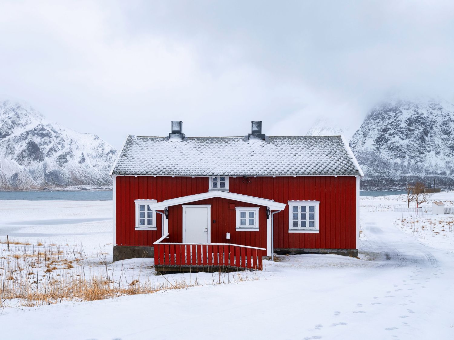 Red wooden cabins in snowy winter landscape with mountains in background.