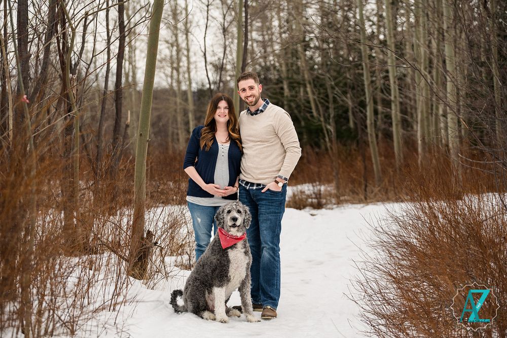 Winter forest engagement photo with couple and their husky dog on snowy trail.