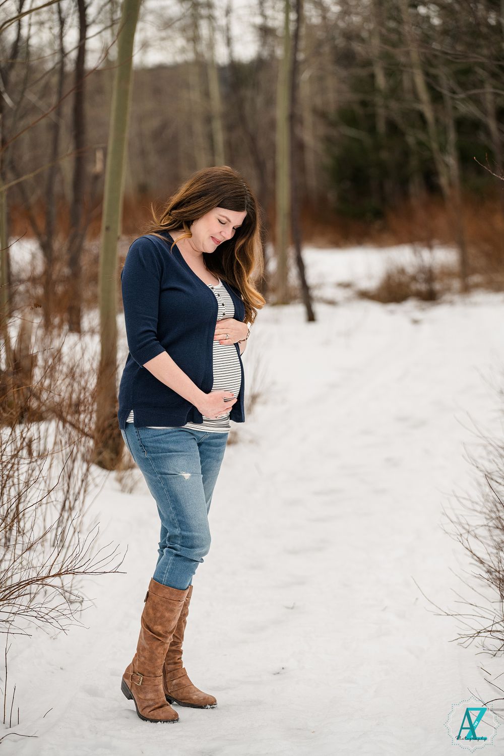 Expecting mother in navy cardigan and brown boots poses outdoors in winter setting.
