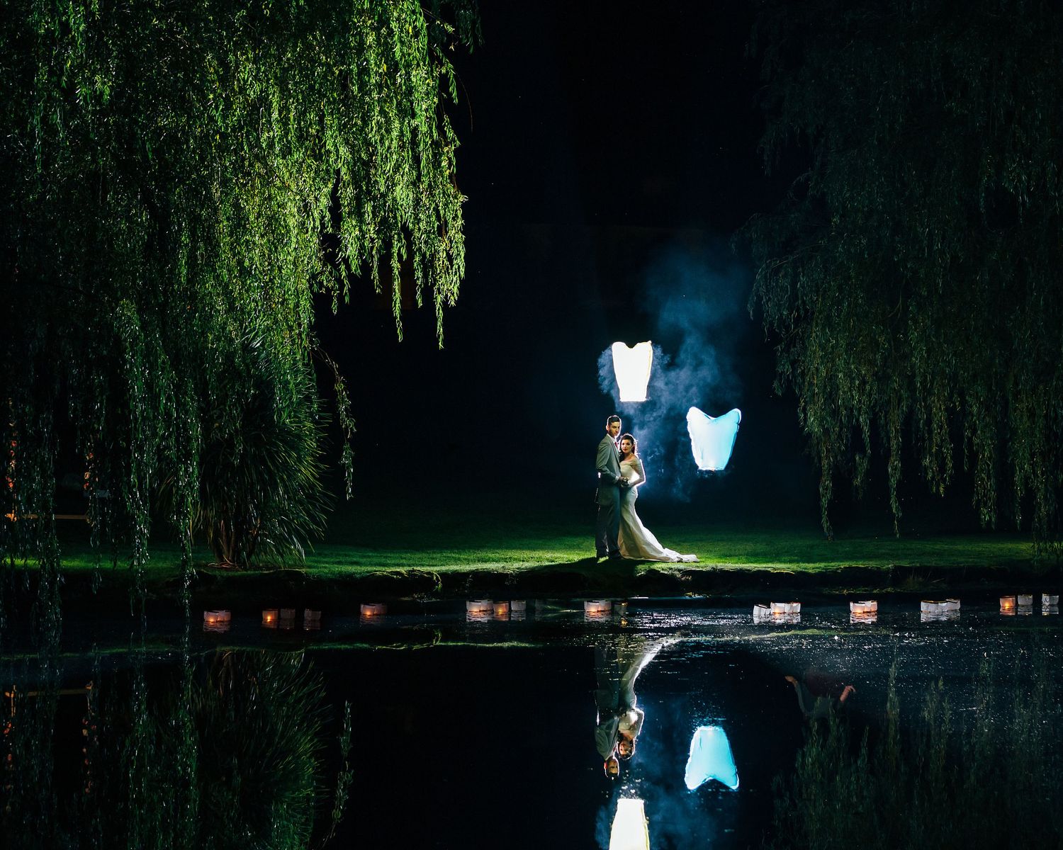 Illuminated wedding dresses glow against dark willow trees in nighttime garden setting at Mount Wolseley.