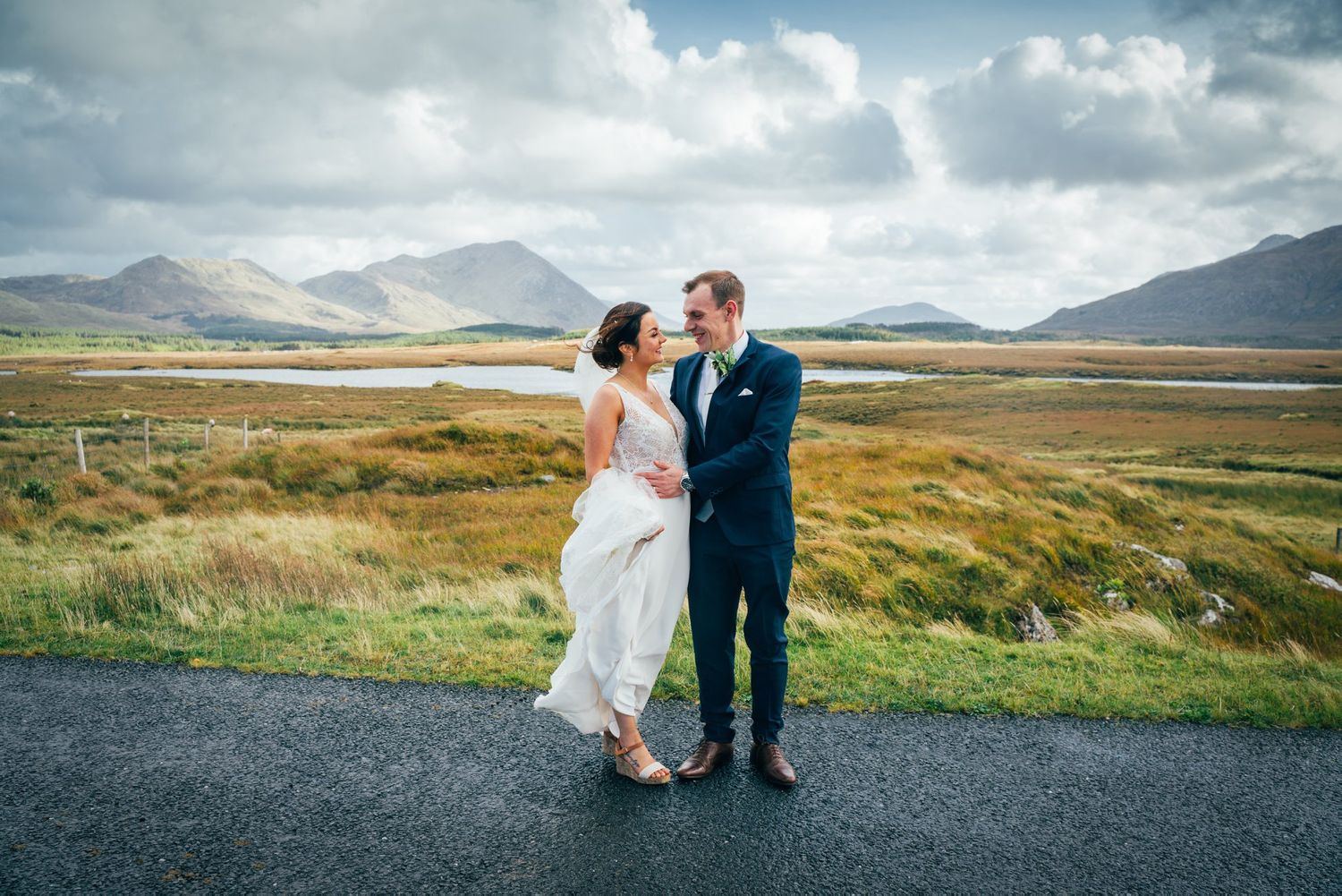 Newlyweds pose together against a dramatic landscape of rolling hills and mountains.