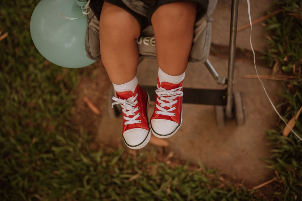 Red converse sneakers on small feet dangling with blue balloon in background.