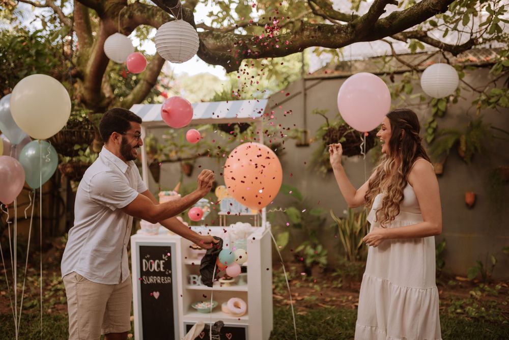 Couple during garden gender reveal celebration surrounded by pink and blue balloons.