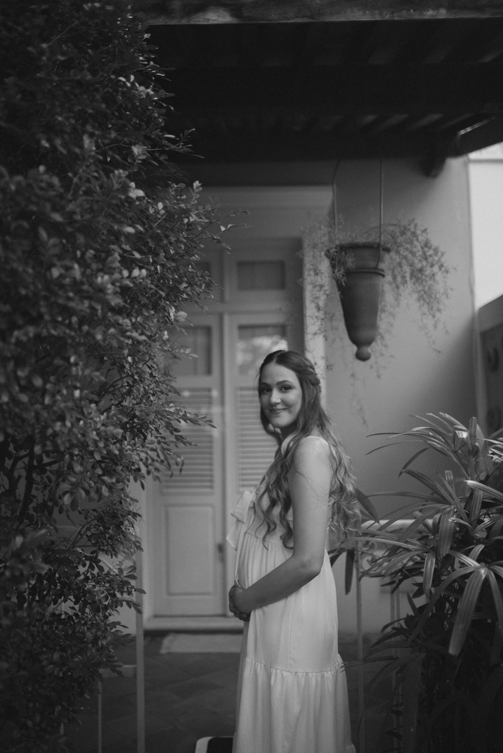 Woman in white dress poses against rustic architecture in dramatic black and white photo.