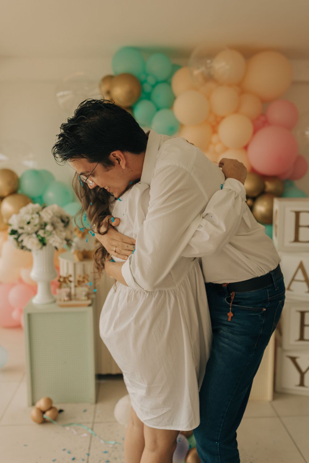Romantic couple embracing at festive party with pastel balloons and decorations in background.
