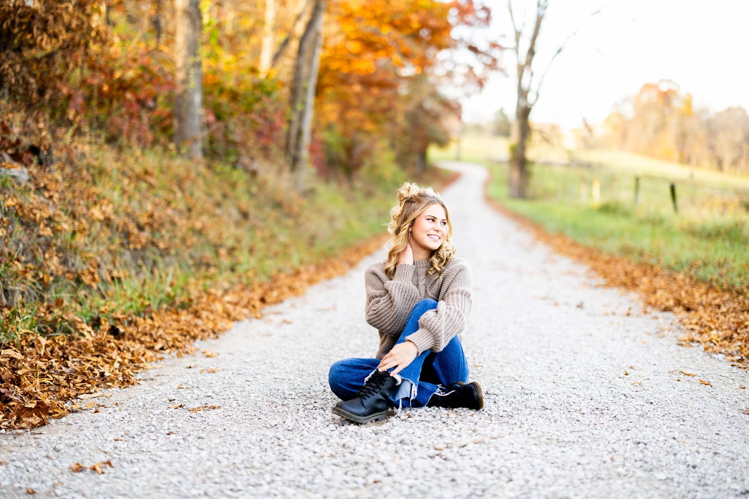 A casual autumn portrait of someone sitting on a gravel path surrounded by fall colors.