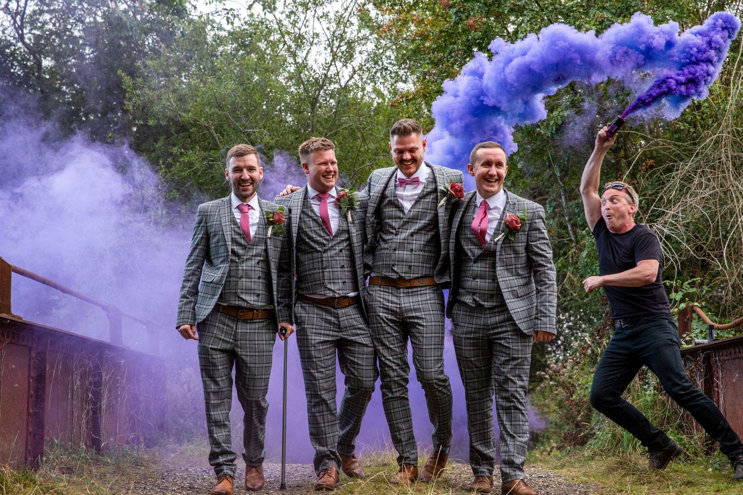Wedding party poses with purple smoke bombs creating dramatic outdoor photo effects.