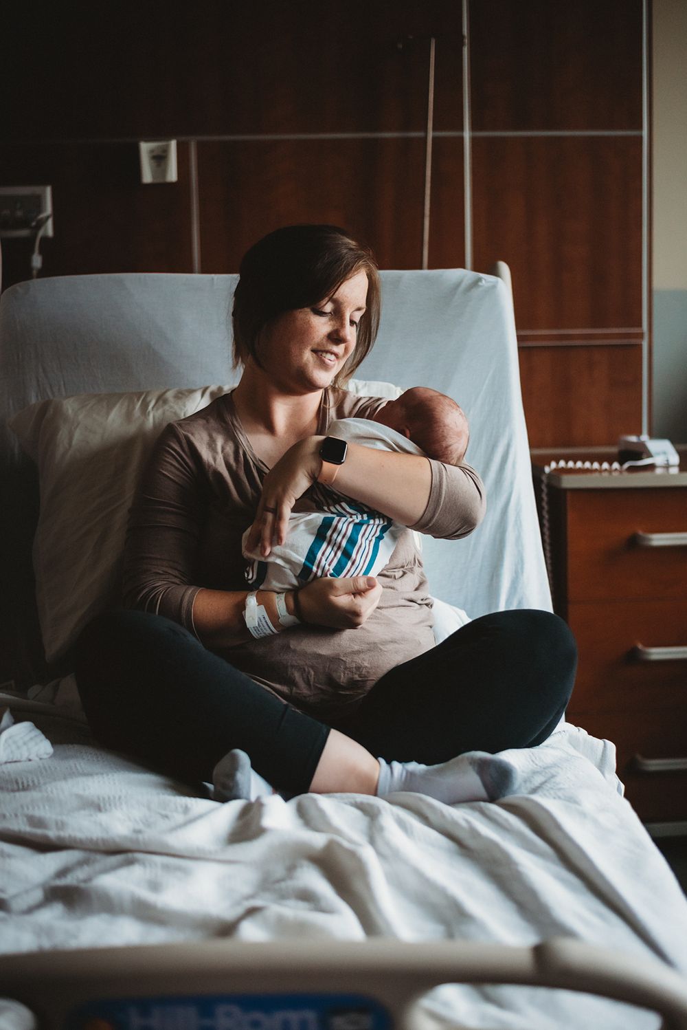 Mom kisses newborn in hospital bed at CHI St. Alexius Health in Dickinson, ND- lifestyle and natural light photographer