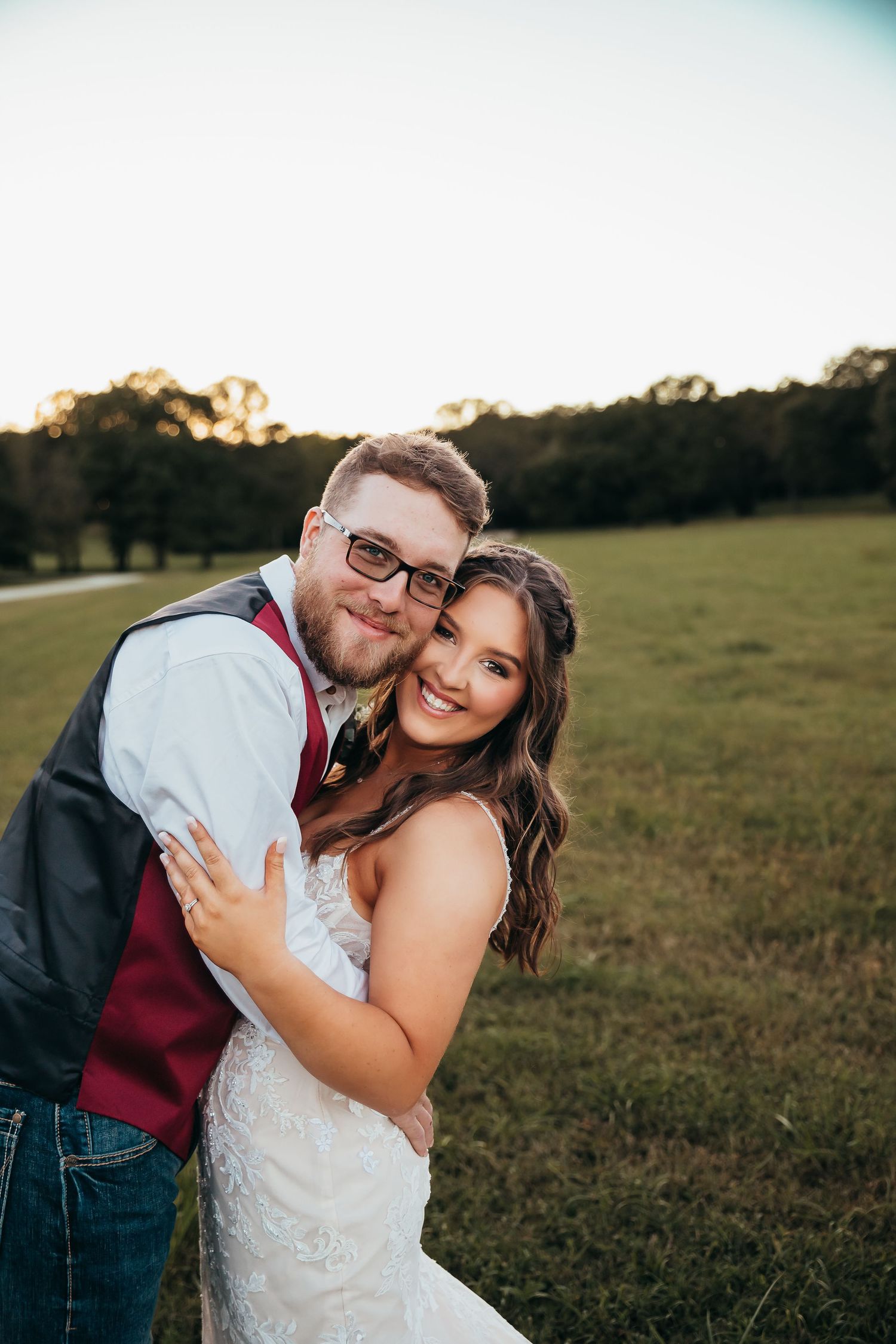 Happy wedding couple embracing outdoors in a field during golden hour sunset.