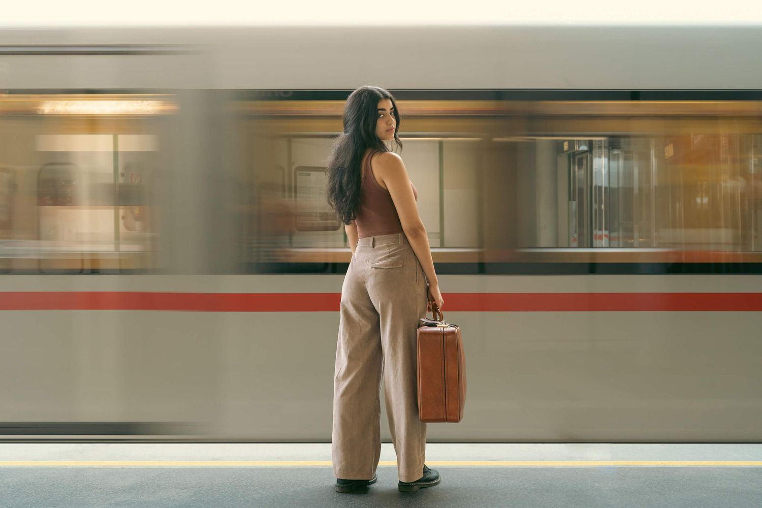 Person with luggage waiting at a subway platform as train passes by with motion blur.