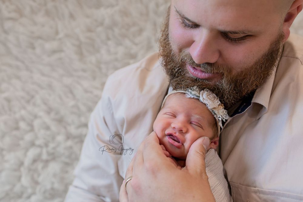 Bearded father gently holding and gazing at his sleeping newborn baby with soft smile.