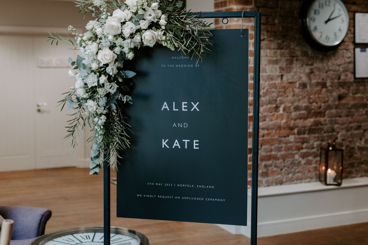 Black wedding signage with white roses and greenery decorating a metal frame.