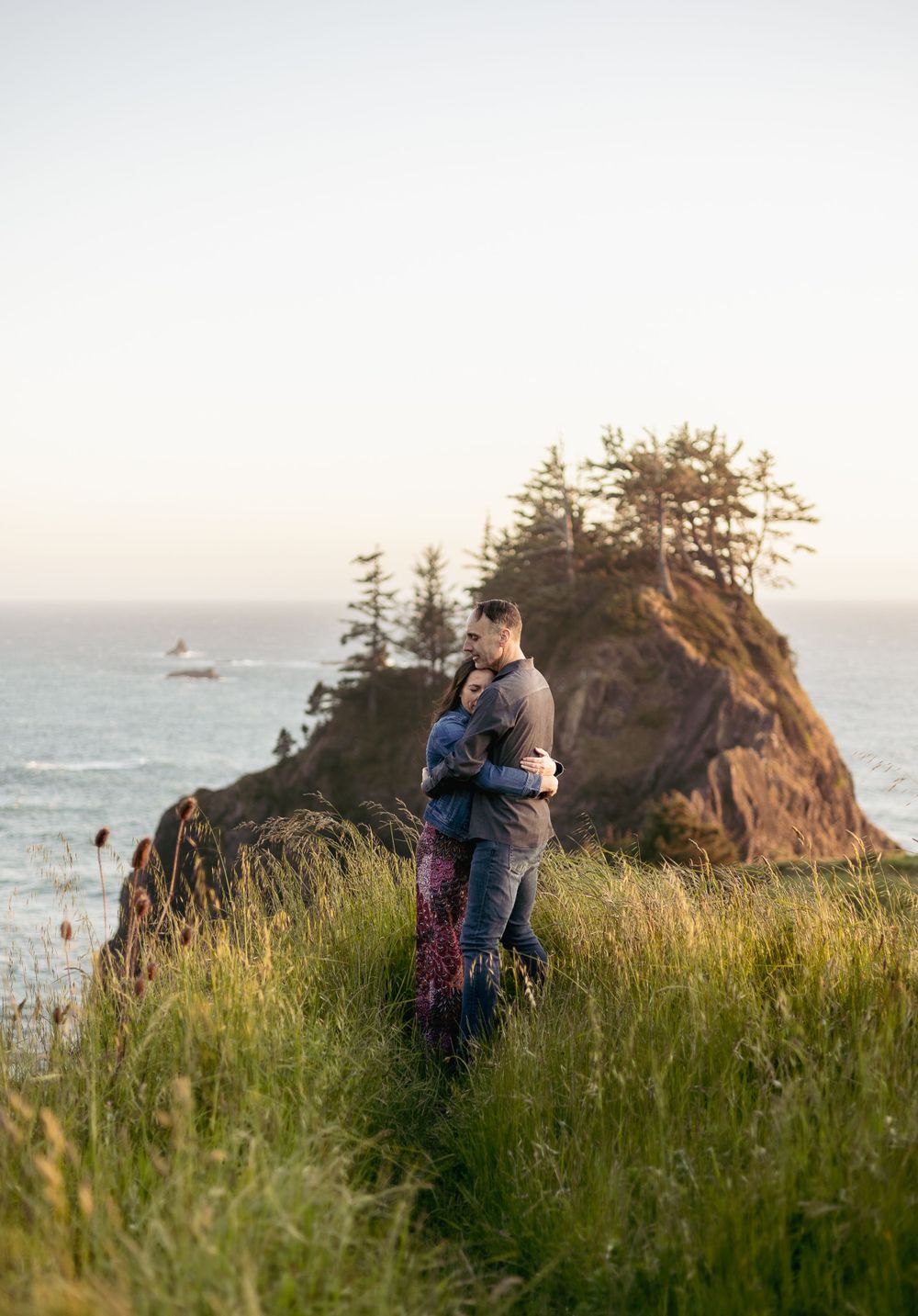 a man and woman embracing on an grassy cliff overlooking the ocean