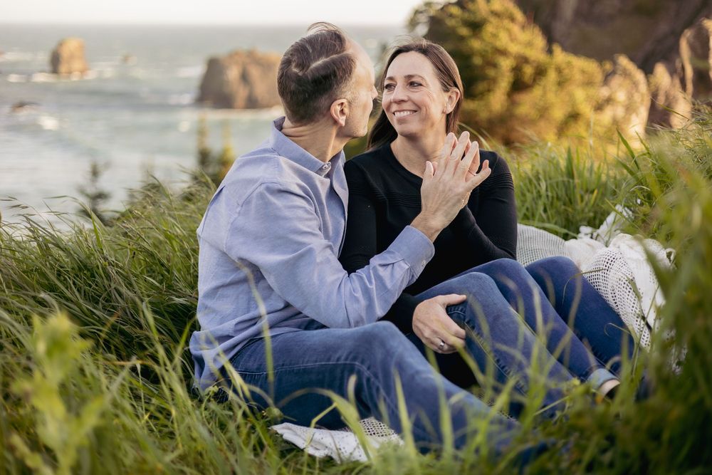a man and woman putting their hands together in a grassy field overlooking the ocean