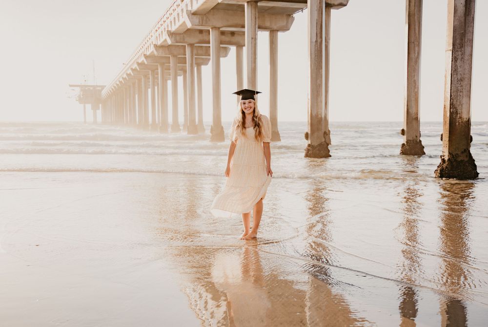 Person in flowing dress walks beneath wooden pier pillars at misty beach.