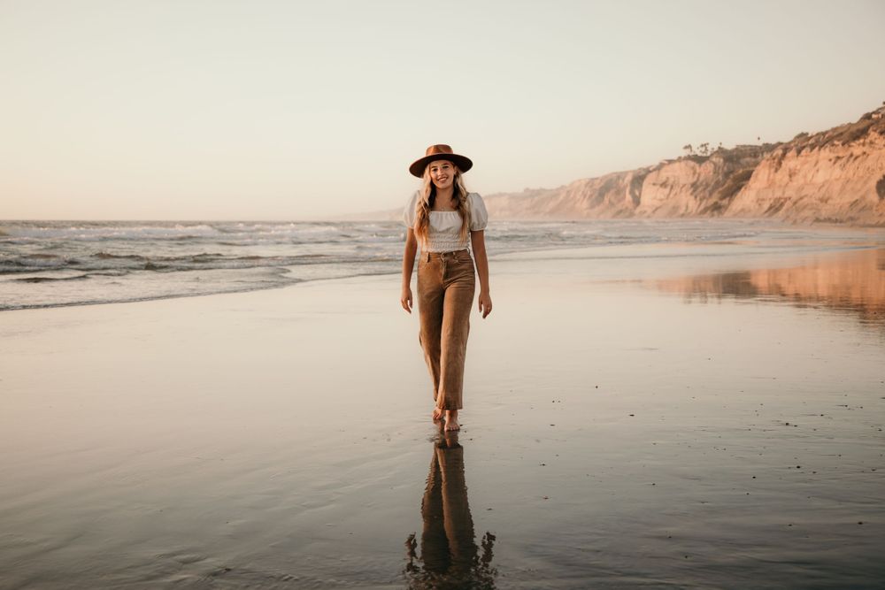 Silhouette walking on reflective beach at sunset wearing wide brim hat.