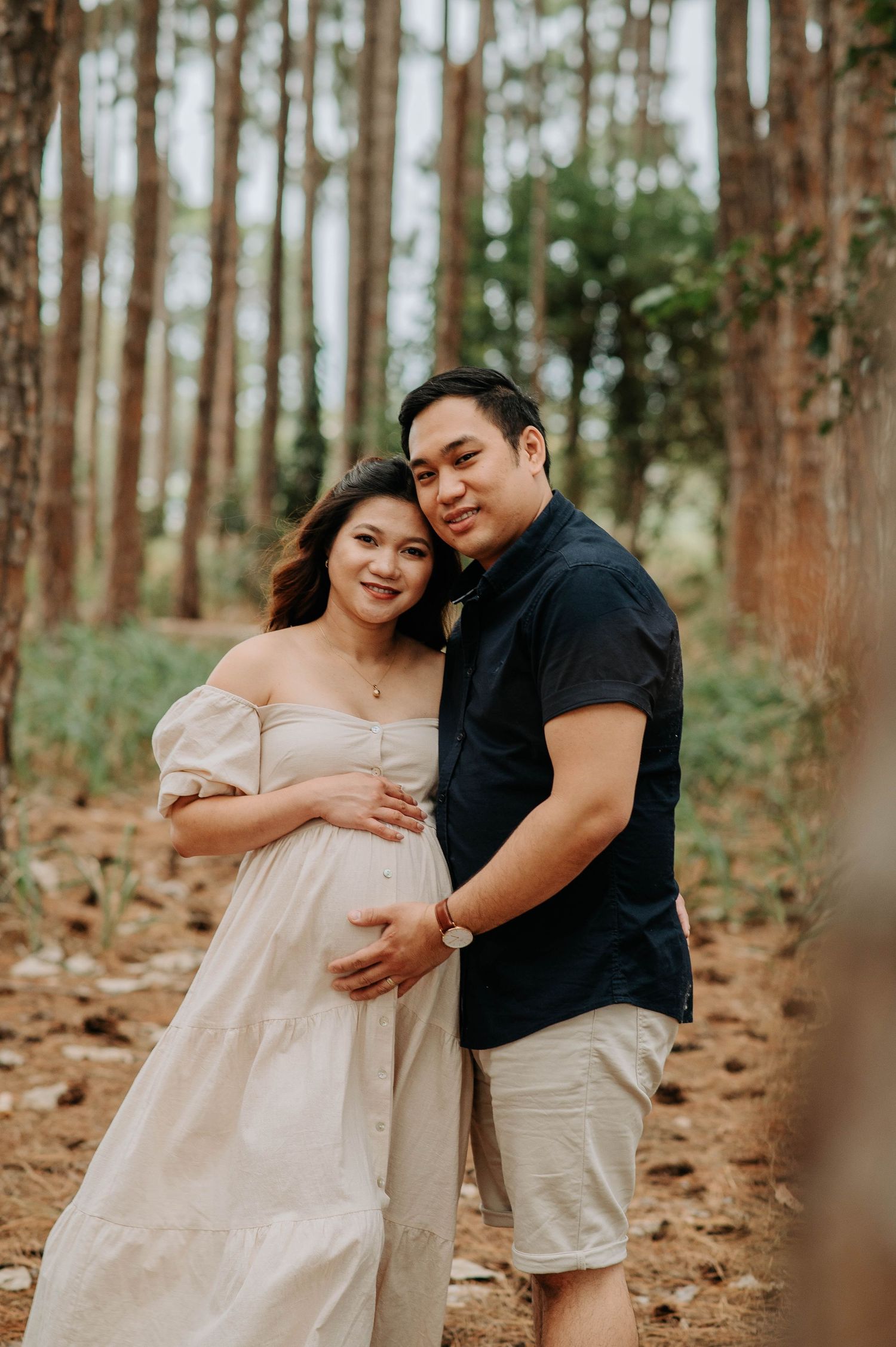 Expecting couple embraces in a romantic maternity photoshoot among pine trees.