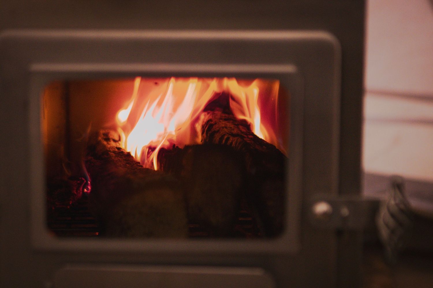 Glowing orange flames visible through glass window of wood burning stove.