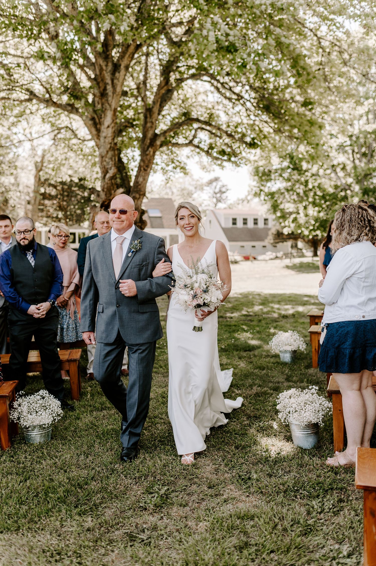 Guests seated on rustic wooden benches during an outdoor wedding with trees in the background.