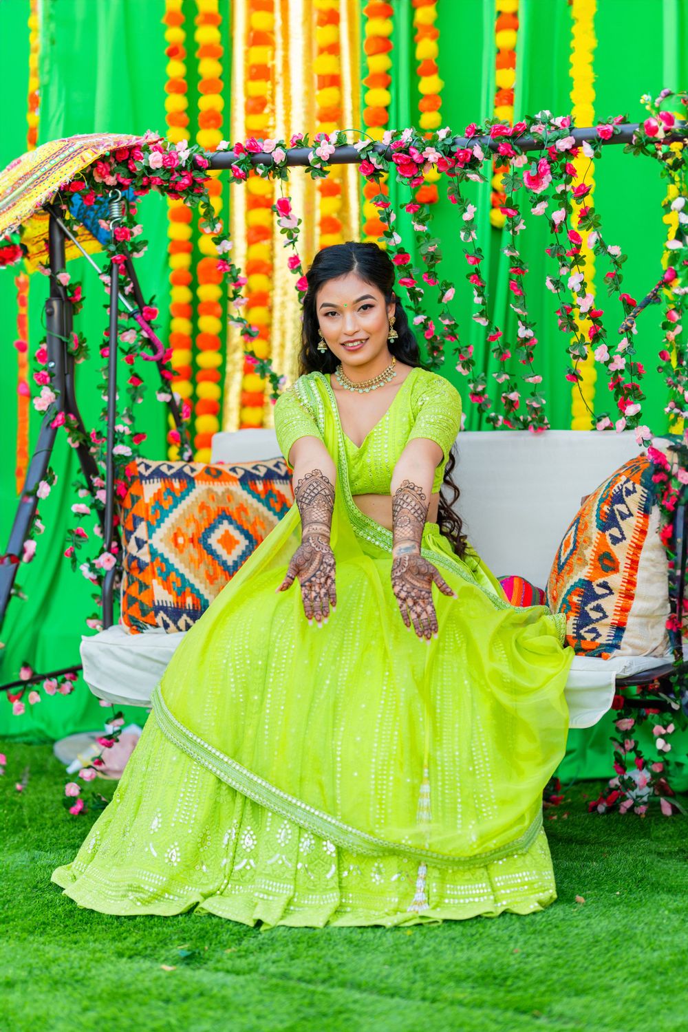 Traditional Indian attire in neon green with henna designs against floral decorations and marigold strings.