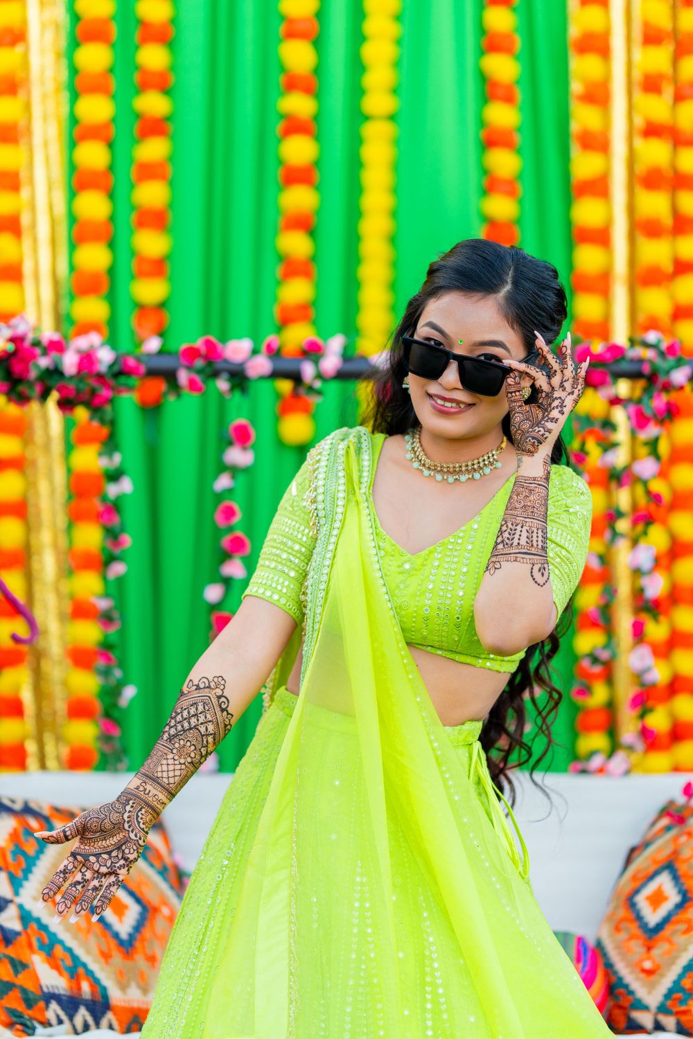 Traditional Indian outfit in neon green with intricate henna designs against marigold decoration backdrop.