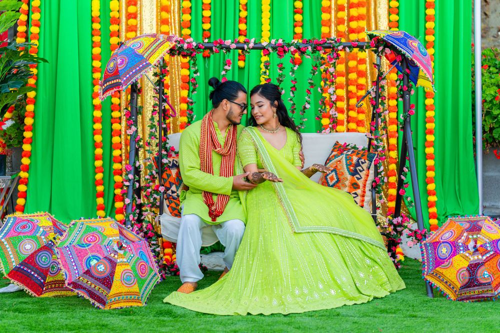 Couple in matching lime outfits seated under decorative umbrellas against colorful backdrop.