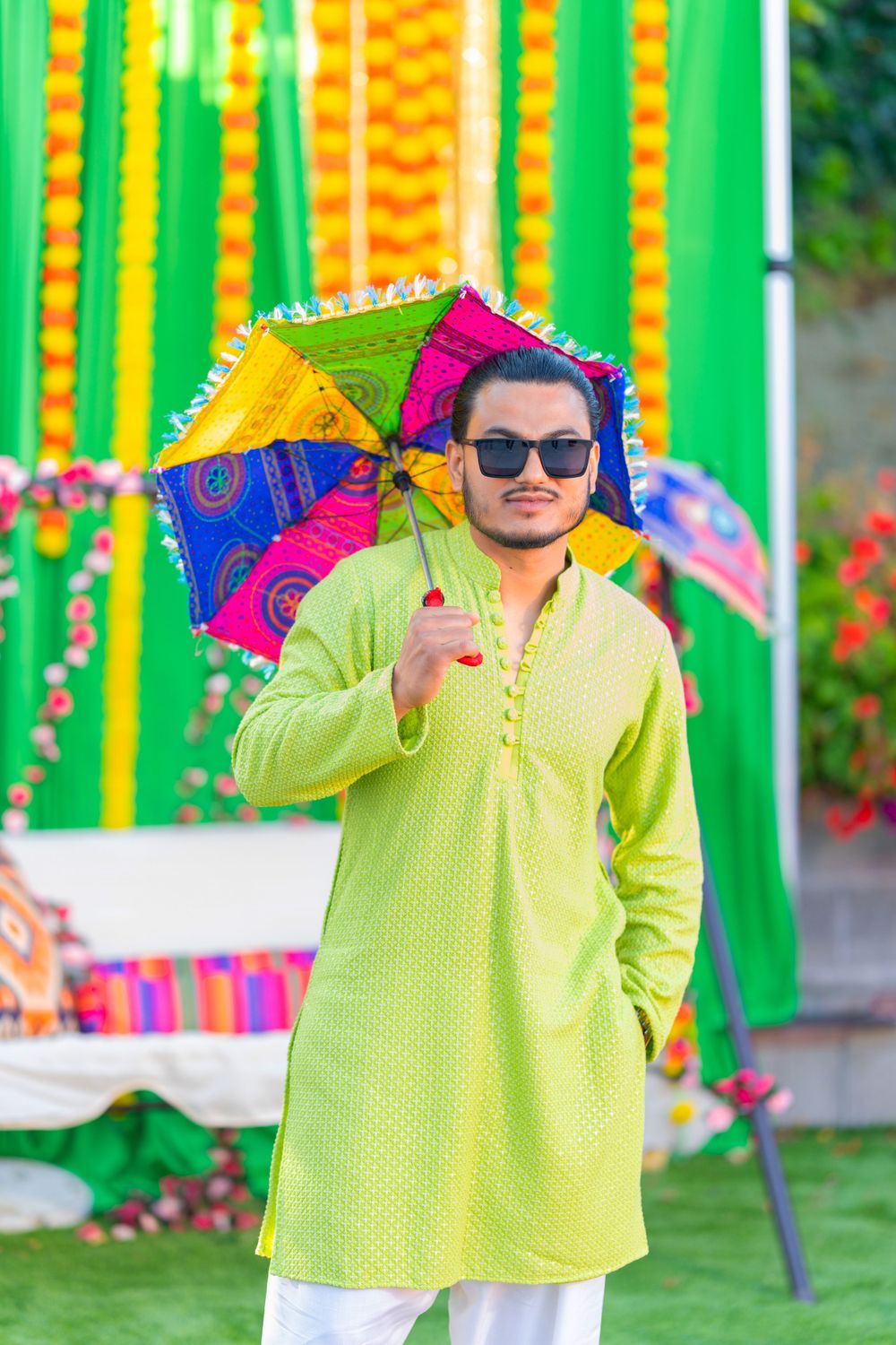 Person in lime green kurta holding colorful umbrella against festive marigold backdrop.