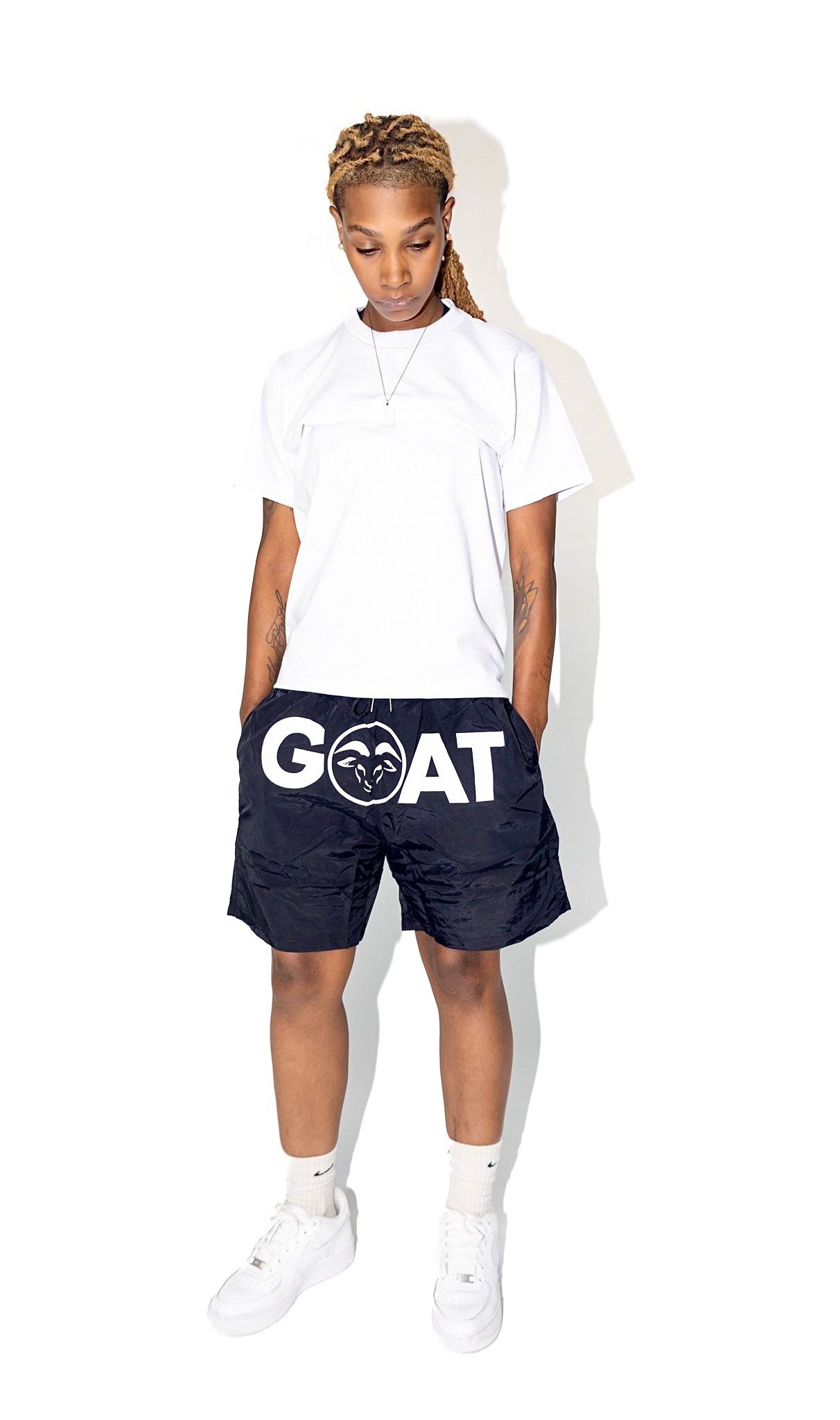 Athletic outfit featuring white t-shirt and navy shorts with GOAT logo on casual streetwear style.