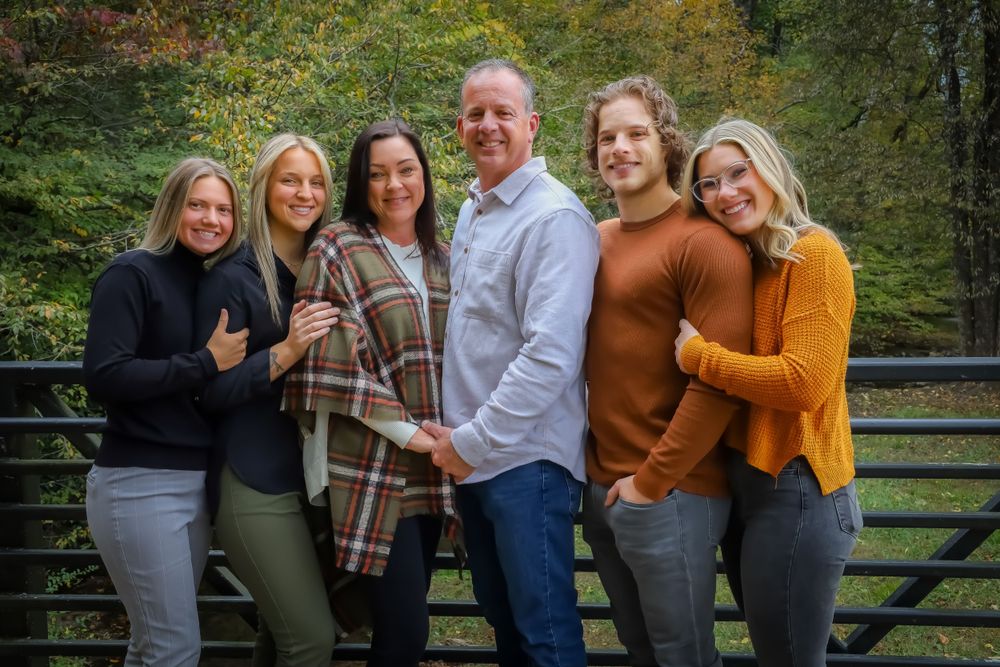 Group photo of family members posed together outdoors with autumn trees in background.