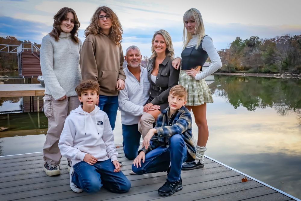 Family sitting together on a wooden dock by a peaceful lake during sunset.