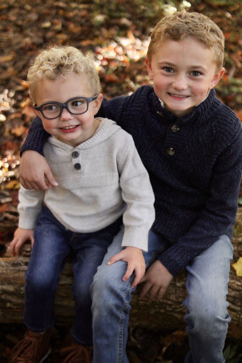 Two young boys in sweaters smile together during fall family photo session.