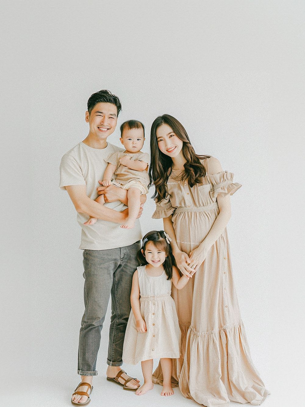 Un portrait en studio d’une famille grandissante portant des tenues coordonnées dans des tons neutres.