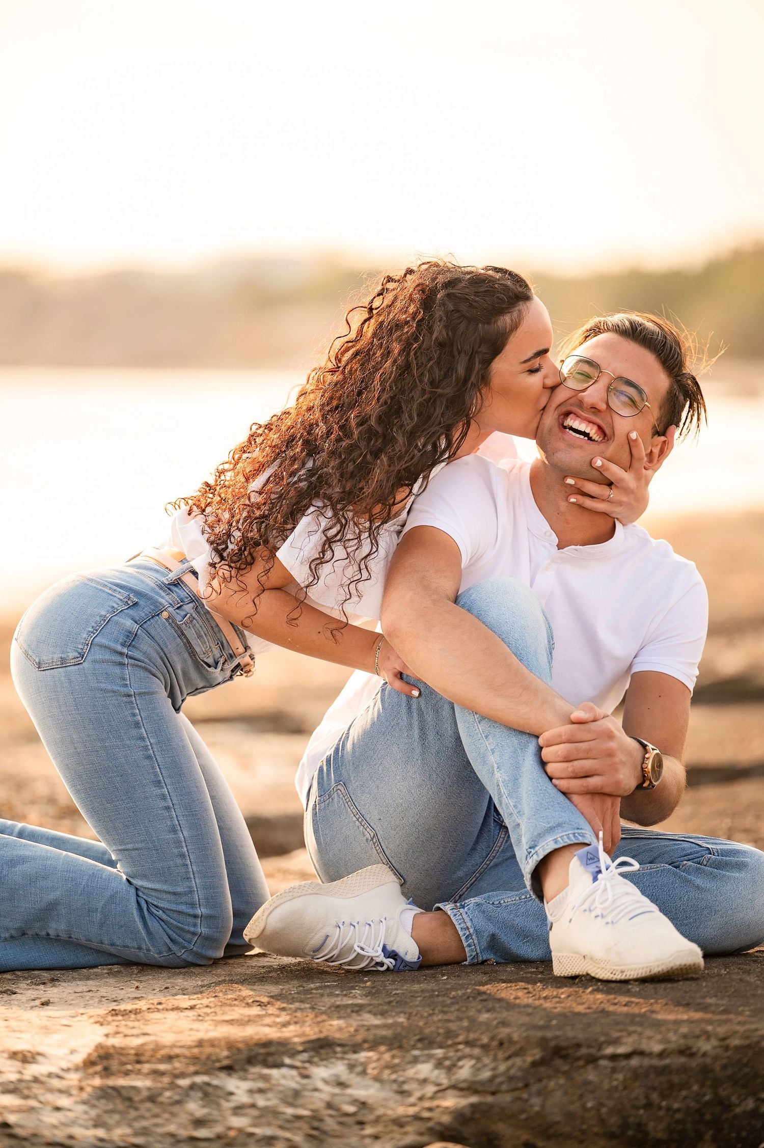Playful couple sharing intimate moment on rocky beach during golden hour sunset.
