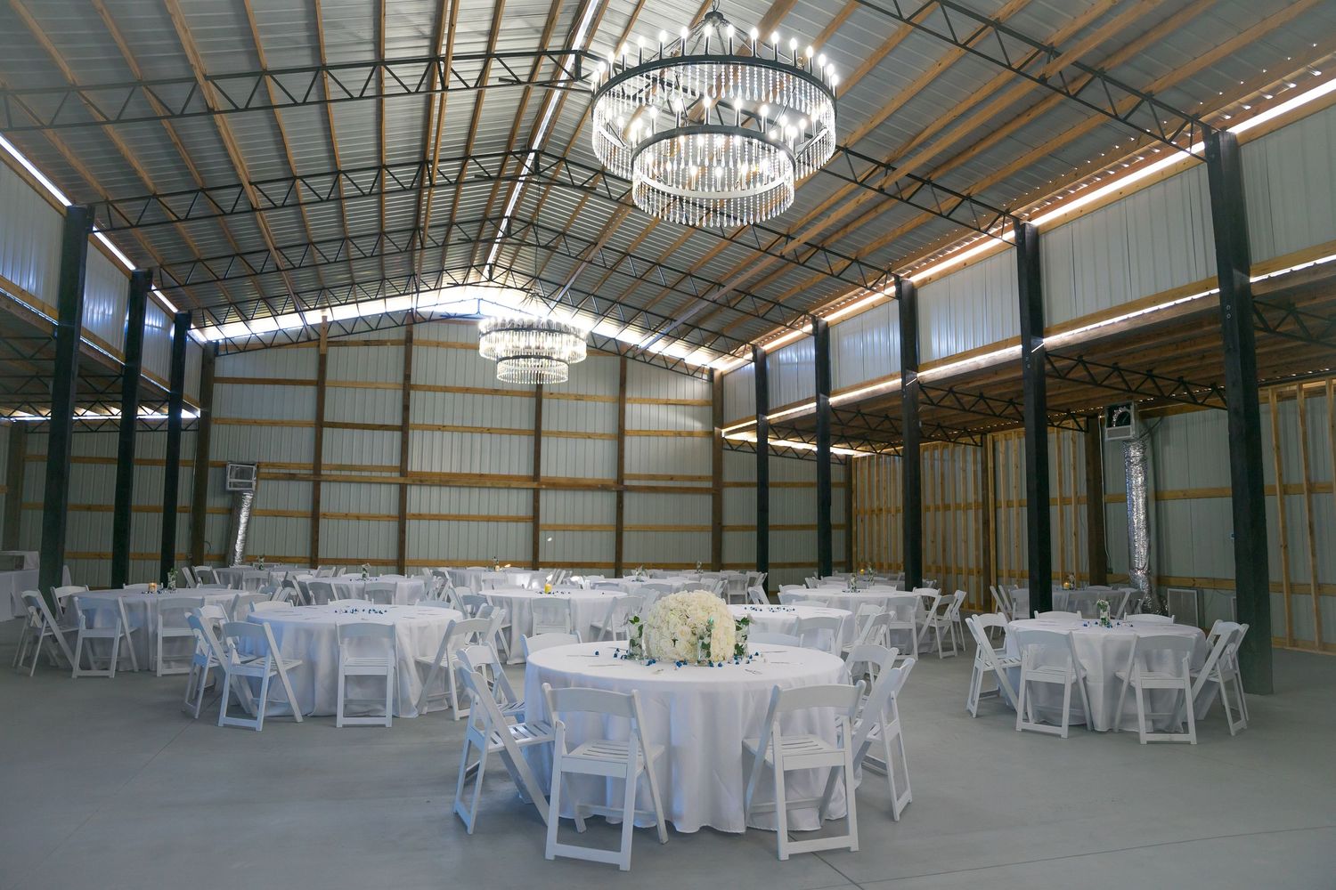 Large indoor wedding venue with white chairs and sparkling chandeliers.