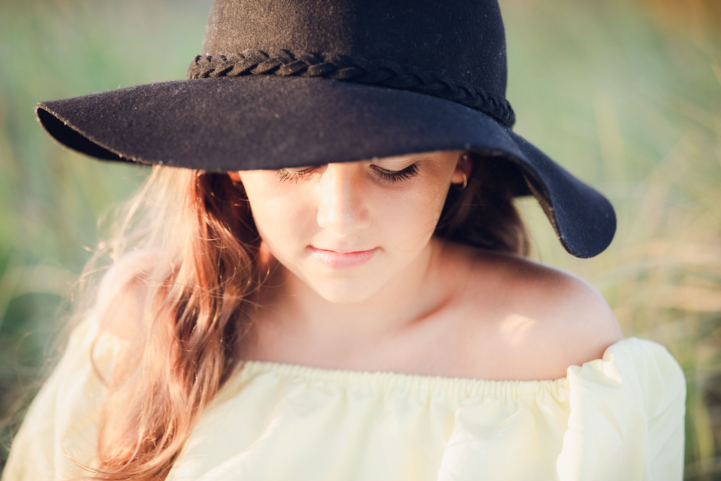 A dreamy portrait of someone wearing a wide-brimmed black hat and off-shoulder white top.