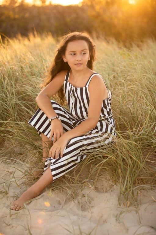 Young girl in striped dress lounging on sandy beach dunes at sunset.