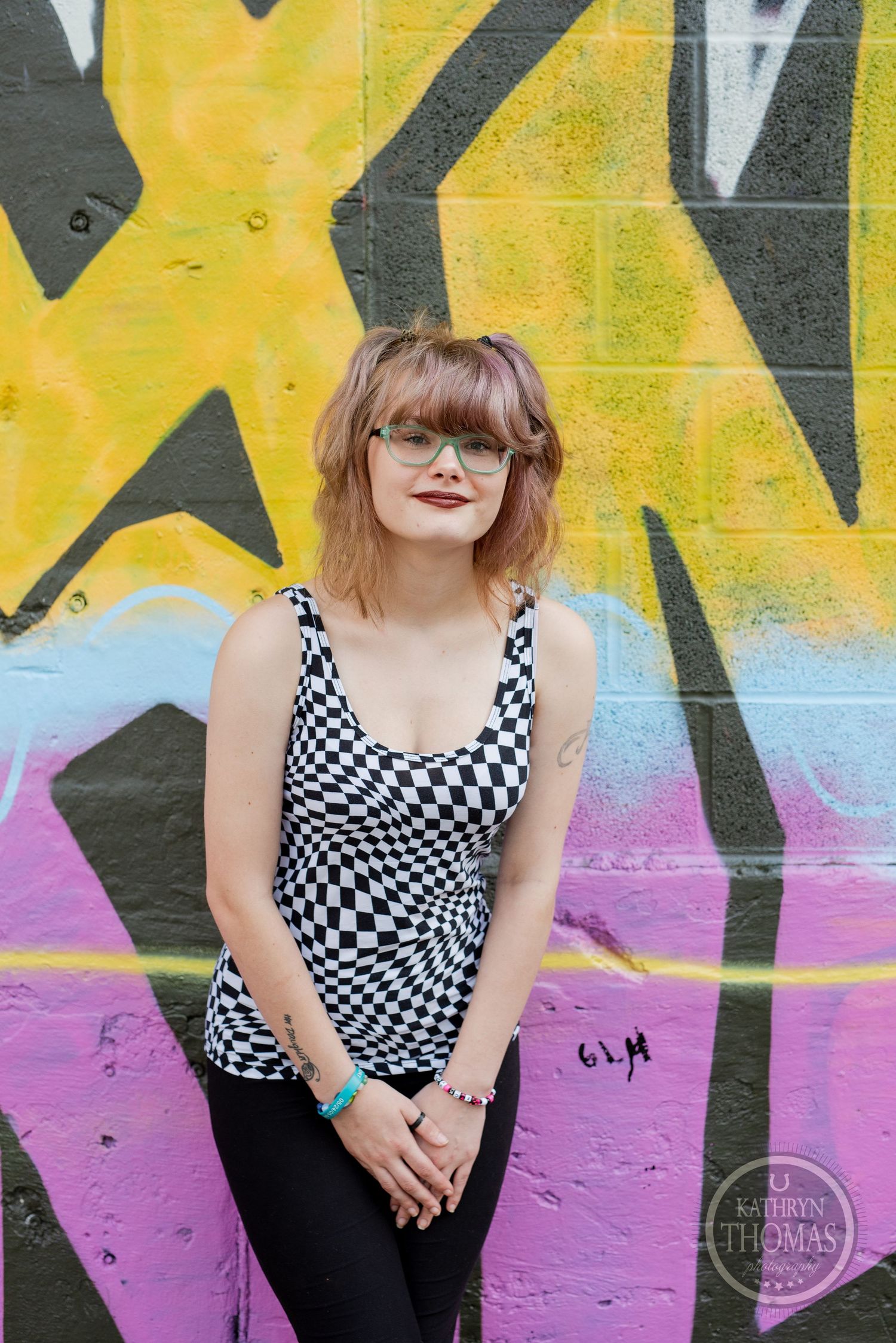 A casual pose against yellow and pink graffiti wall wearing checkered tank top.