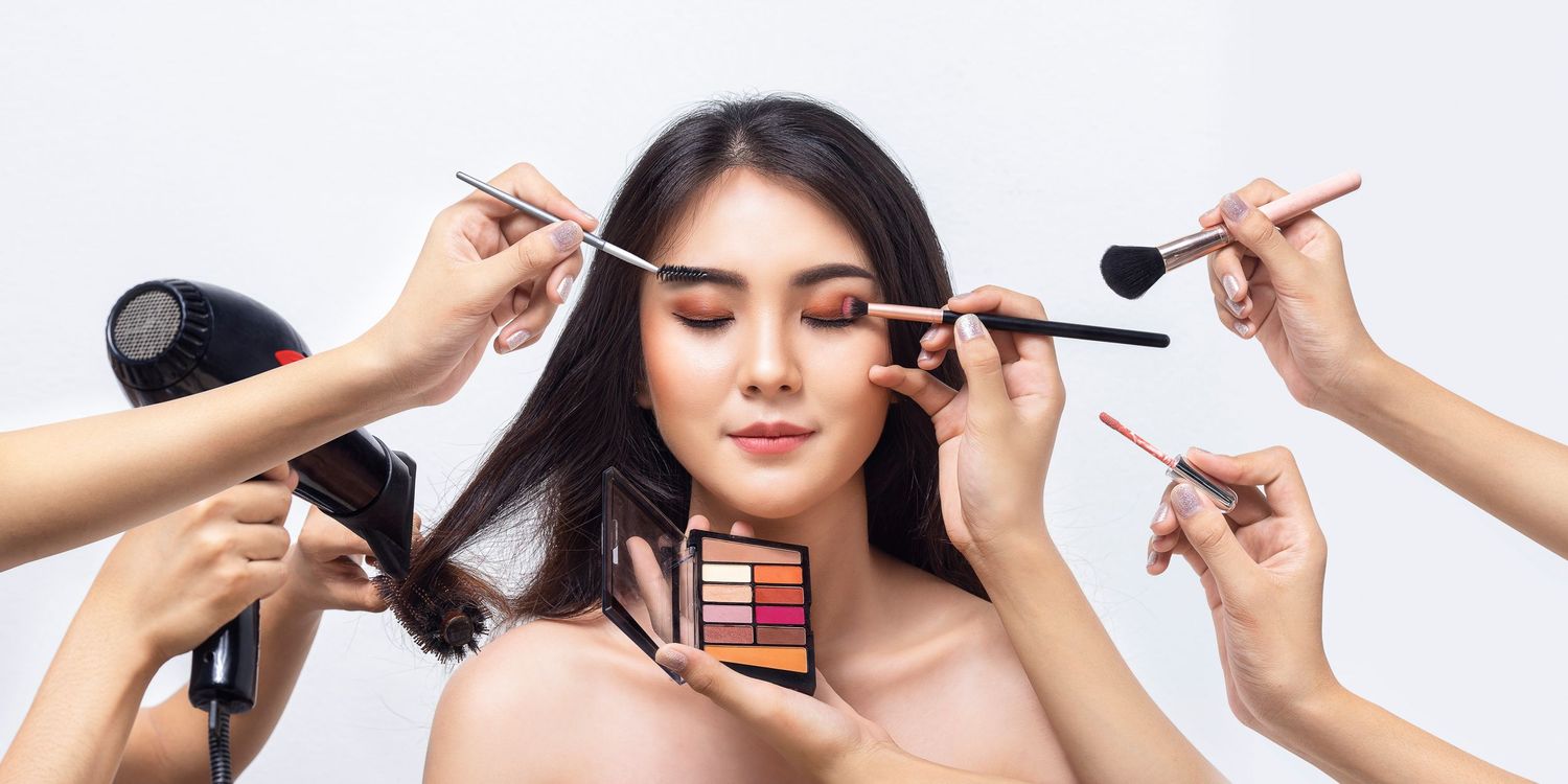 Hands holding makeup brushes and cosmetics around a model during beauty preparation.