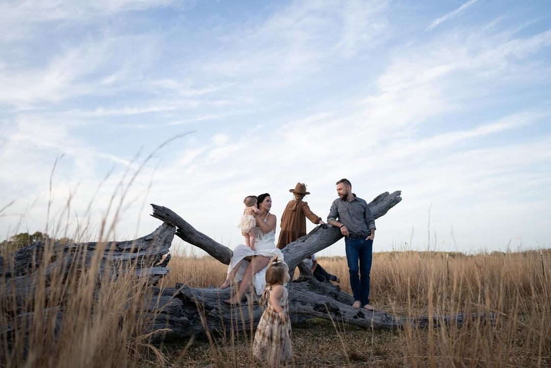 Family silhouettes against blue sky walking through tall grass in a field.