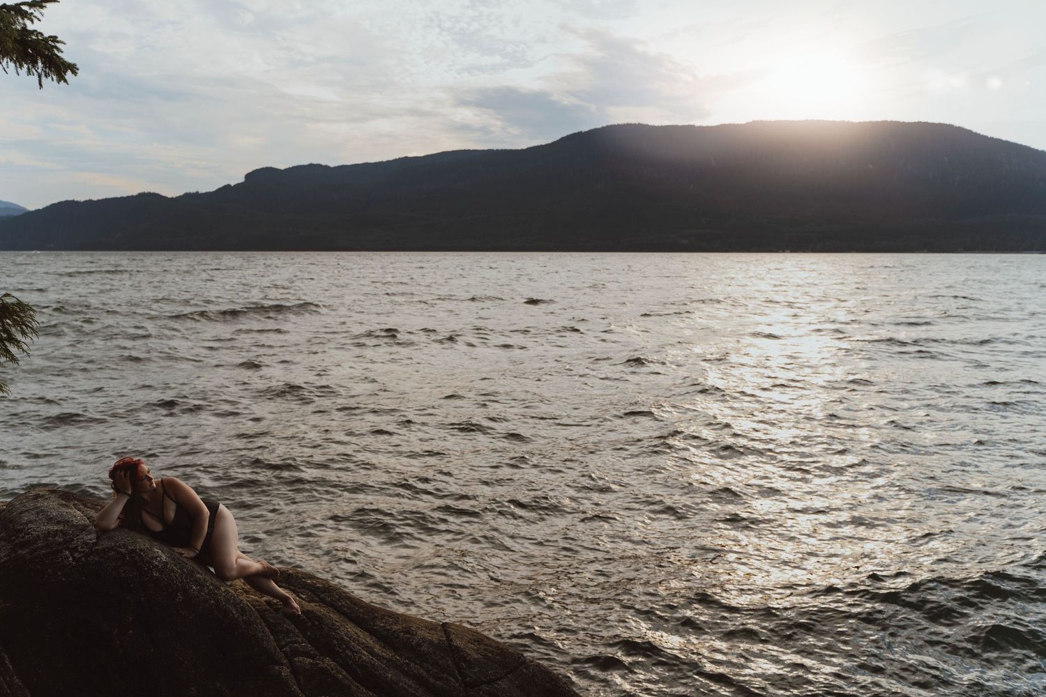 Sunset view over a lake with mountains and silhouetted rocks in the foreground.