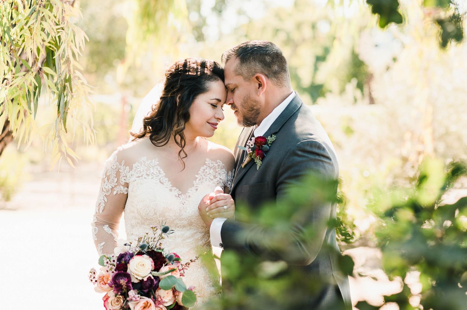 Romantic wedding portrait among willow trees with soft natural lighting.