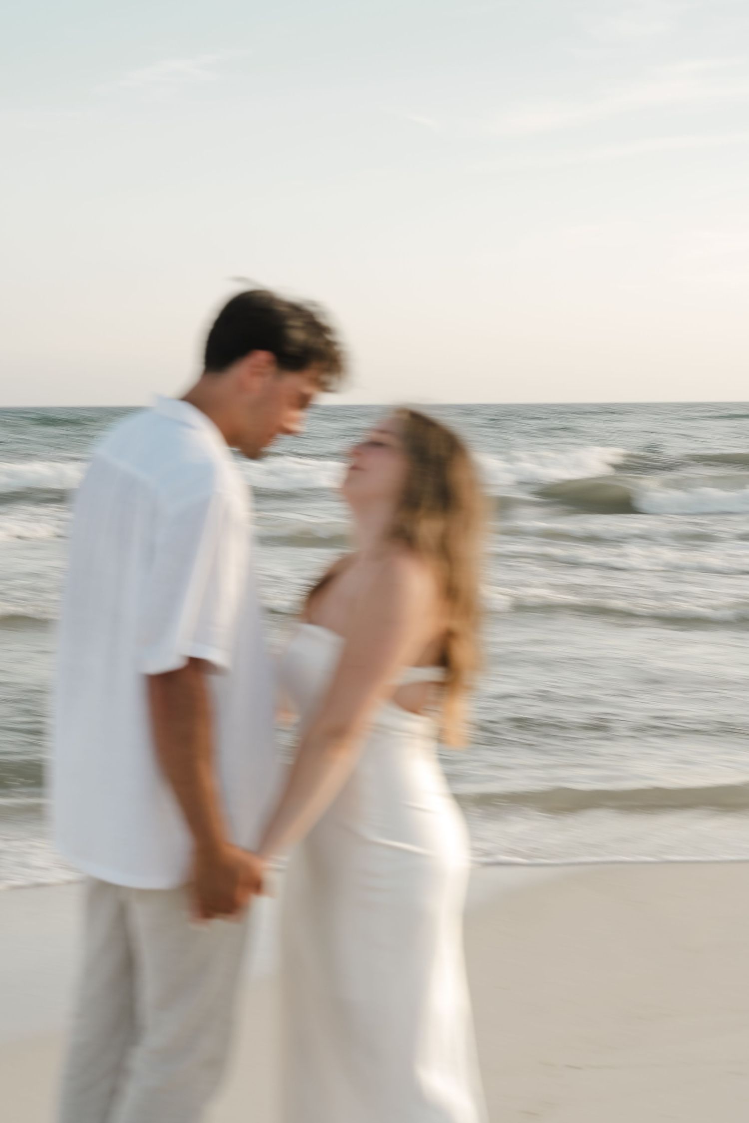 Artistic motion blur photo of couple in white clothing on beach at sunset.