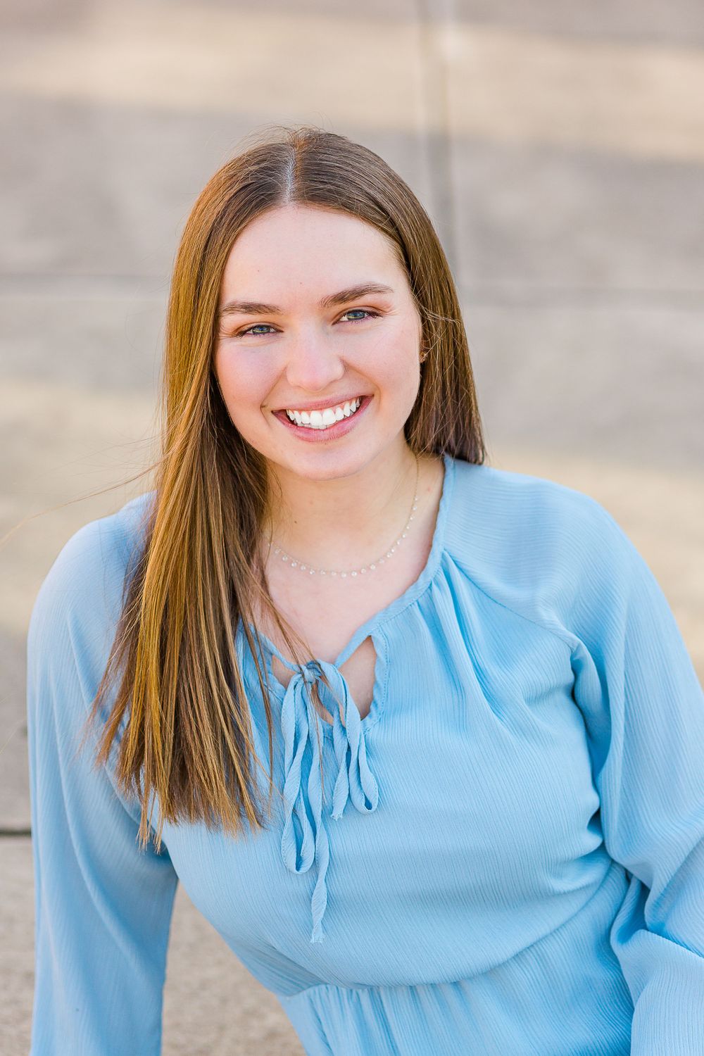 A light blue long-sleeve top with tie neckline detail against a neutral background.